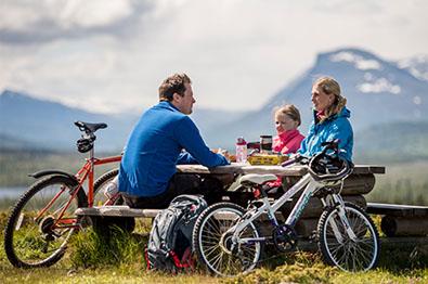 Eine Familie mit Fahrrädern rastet an einer Bank|