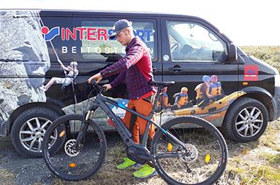 A person with an e-bike is standing in front of a van with the Intersport logo imprinted