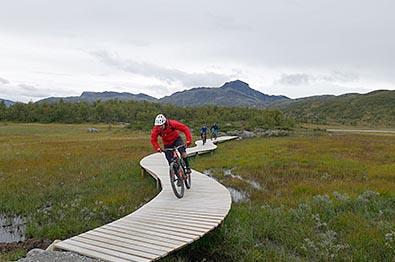 Tre syklister på et teknisk element langs en terrengesykkelløype på fjellet.