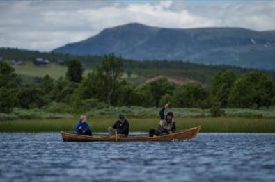 Three people fishing from a boat on a lake.