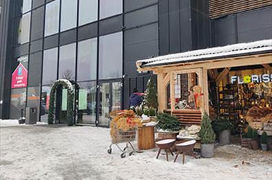 Inngangsparti til et kjøpesenter med koselig trebod for blomsterbutikk