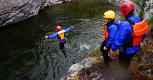 Eine Person springt von einem Felsen in ein Flussbecken, wobei zwei andere zusehen.