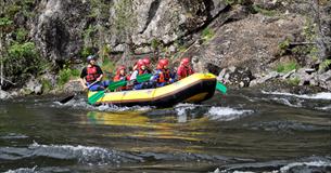 Ein gelbes Raftingschlauchboot auf einem Fluss passiert einen Felshang