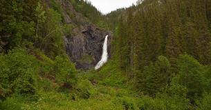 The waterfall Juvfossen falls over a rocky cliff surrounded by lush green vegetation.