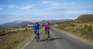 Zwei farbenfroh gekleidete Radfahrer auf breiter Schotterstraße in freliegendem Hochland unterwegs auf der Stølsvidda entlang des Mjølkevegen.
