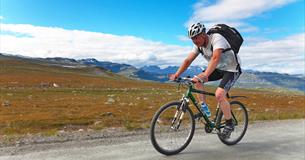 Radfahrer auf dem Slettefjellvegen mit Jotunheimens Bergen im Hintergrund.
