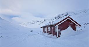 Kleine rote Berghütte im winterlichen Gebirge mit Skiern an der Hüttenwand