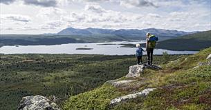Woman an child standing on a small rock enjoying a magnificent view towards a lake and mountains in the far distance.