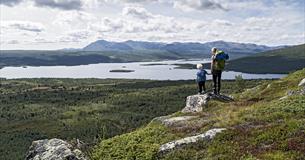 Woman an child standing on a small rock enjoying a magnificent view towards a lake and mountains in the far distance.