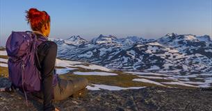 Women up close seen from behind while enjoying view towards snow patched mountains.