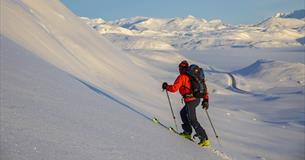Person på vei opp fjellside med randoneeski, vid utsikt over snødekt fjellandskap