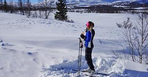 Eine Skiläuferin genießt eine Brause in der Frühlingssonne im Loipennetz bei Kvålestølen. Ein Berg im Hintergrund.