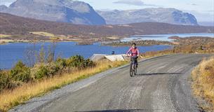 Fahrradfahrer auf einer unbefestigten Straße mit Seen un Bergen im Hintergrund