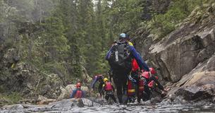 En gruppe personer i våtdrakter og hjelmer går i en elv.