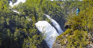 Double waterfall in a summergreen birch valley.  A person standing at the abyss.