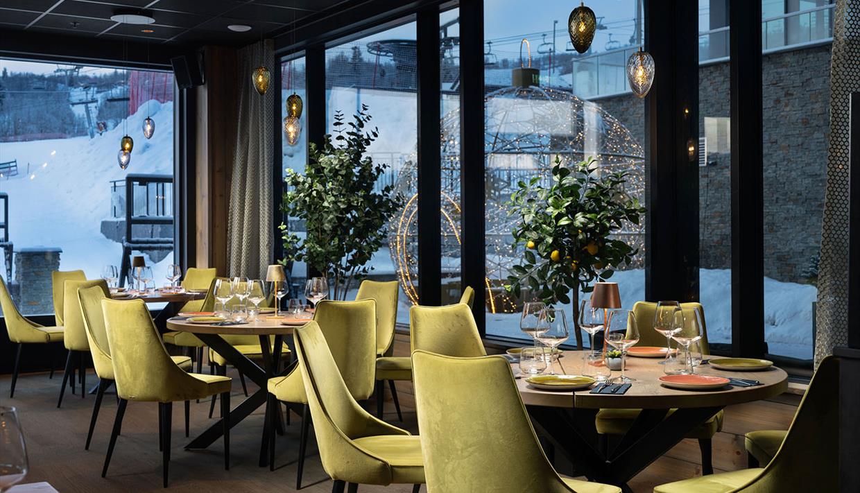 Restaurantinnredning med lysegrønne polsterstoler og varm belysning. Ute er det snø.