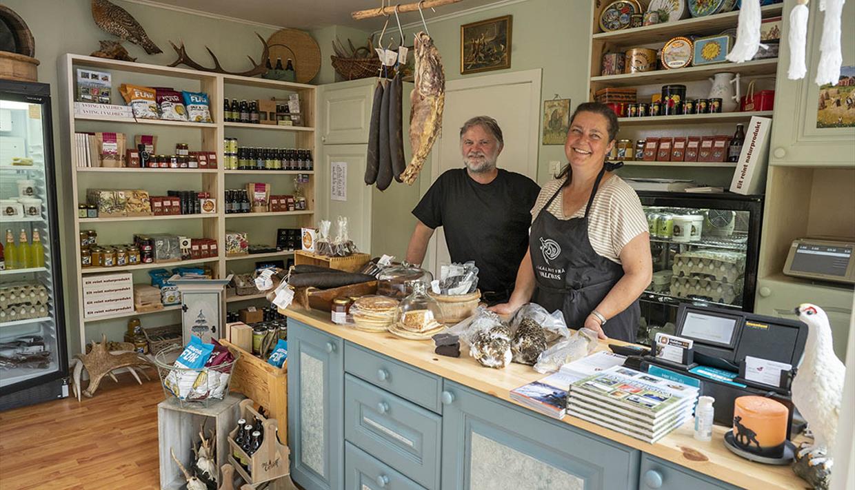 The owners of the store standing behind the counter of the small, cosy shop.The shelves are filled with delicious local food.
