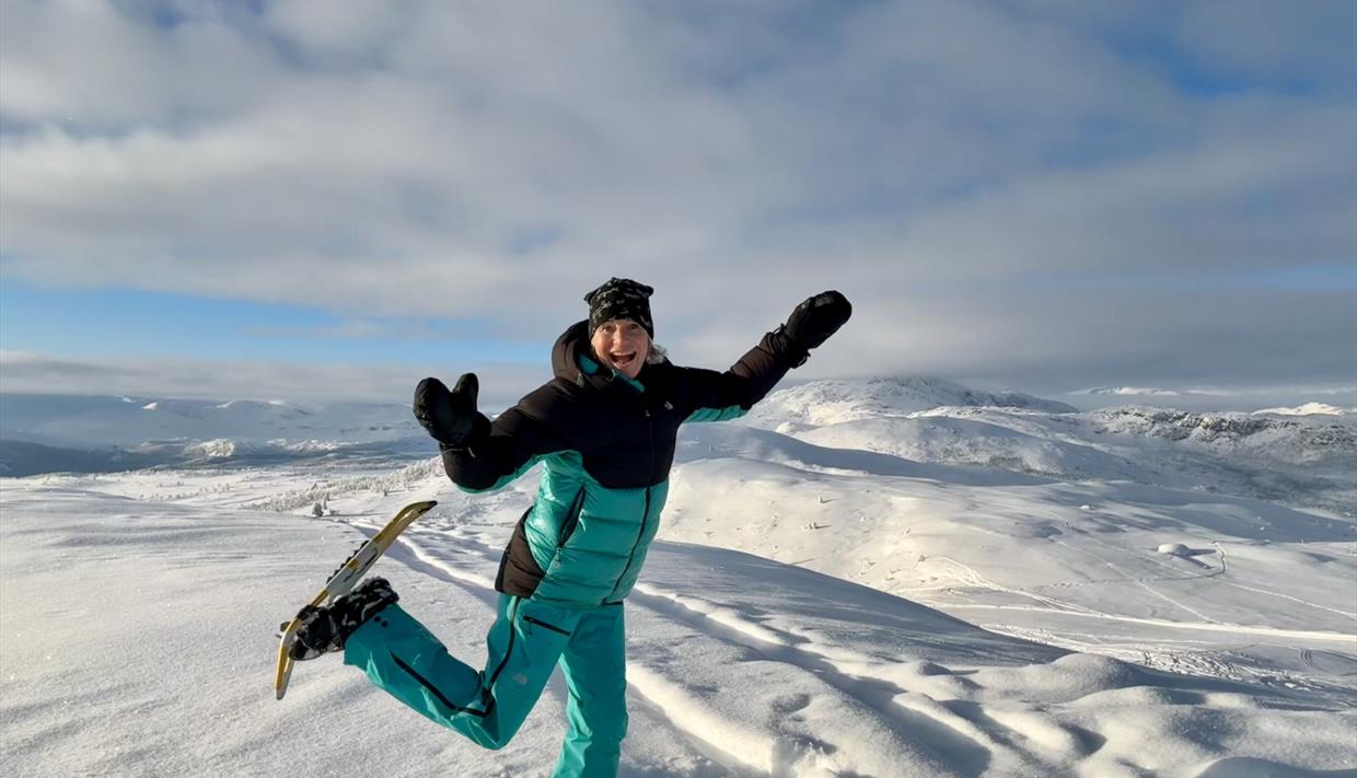 Viser en glad person på truger på et vinterkledd fjell.