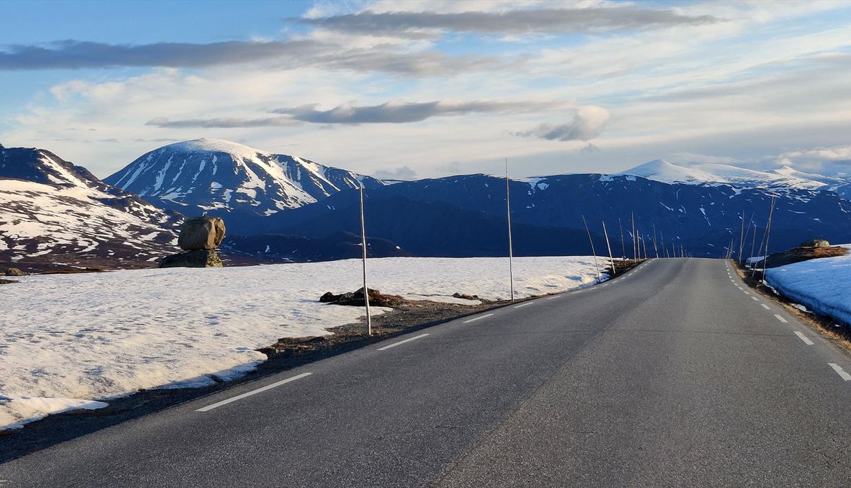 Road over mountain plateau with snow-covered peaks in the background.