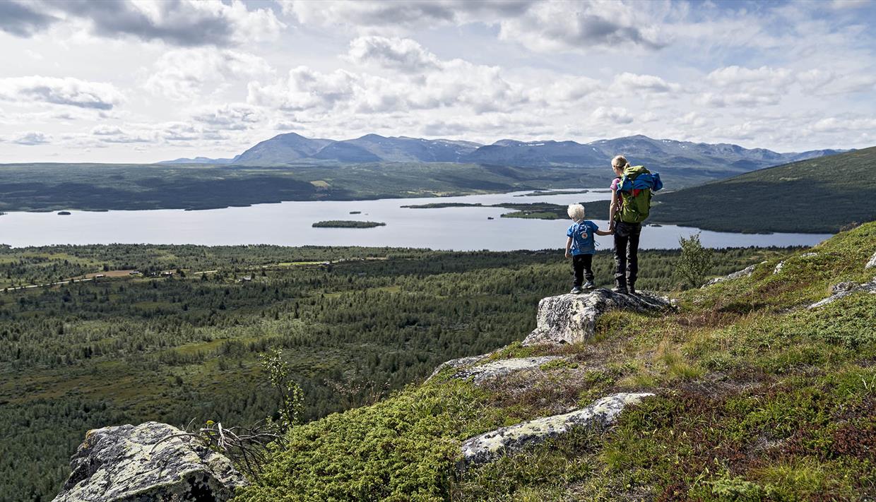 Woman an child standing on a small rock enjoying a magnificent view towards a lake and mountains in the far distance.