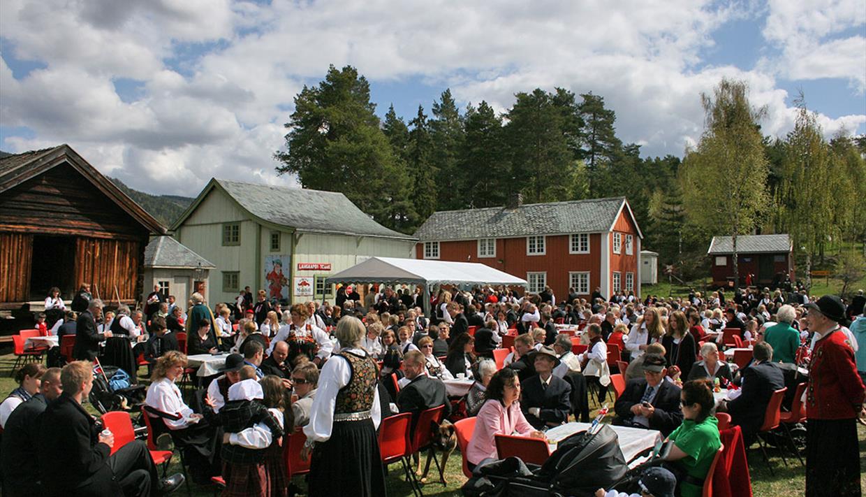 Folkemengde ikledd bunad, blant gamle hus på Valdres Folkemuseum