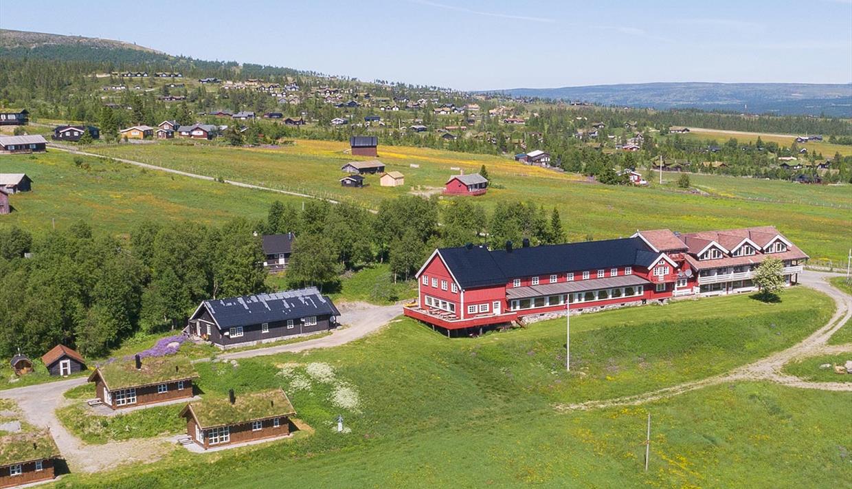 Dronenfoto eines roten Holzhotels in einer grünen Wiesenlandschaft