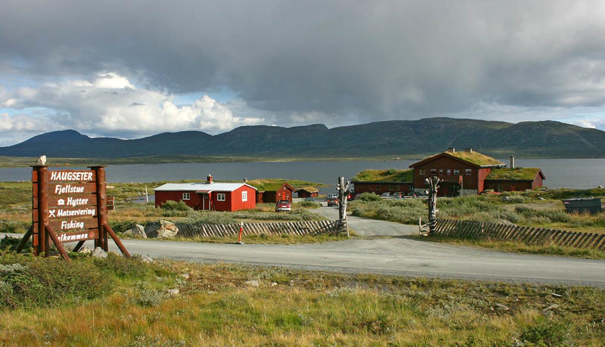 The mountain lodge Haugseter Fjellstue with a grass roof on the shore of Lake Vinstre. Mountains and dark clouds in the backgriund.