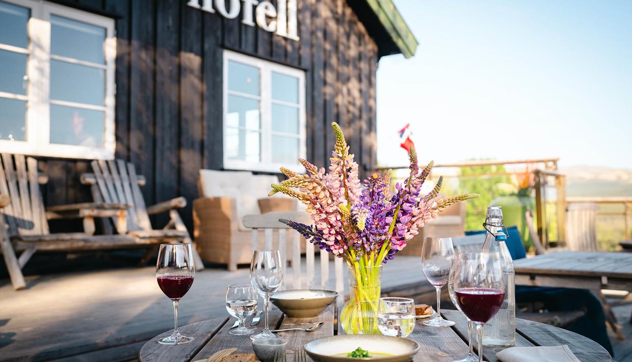 Stilvoll eingedeckter Holztisch mit Blumenstrauß auf der sonnigen Terrasse des Skåbu Fjellhotels