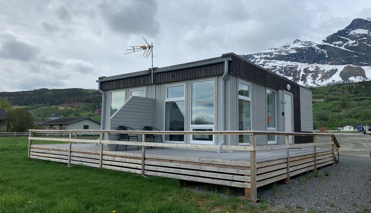 Ein kleines, viereckiges Gebäude mit Apartments, einer rundumgehenden Veranda und Bergen im Hintergrund