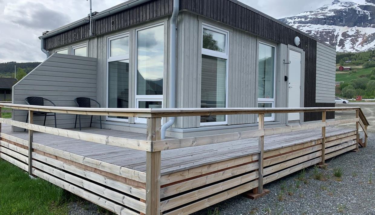 Ein kleines, viereckiges Gebäude mit Apartments, einer rundumgehenden Veranda und Bergen im Hintergrund