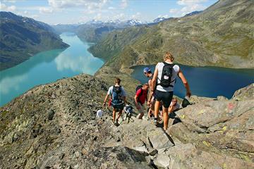 Turgåere på vei ned den bratte eggen. Utsikt mot fjell i Jotunheimen og Gjendefjorden.