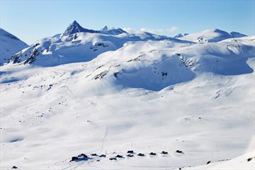 En liten fjellstue og et knippe hytter i et nedsnødd høyfjellslandskap fra fugleperspektivet