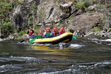 Ein gelbes Raftingschlauchboot auf einem Fluss passiert einen Felshang