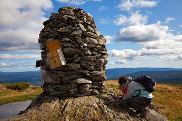 A large summit cairn on Synet. A mother and a child register their trip in the tour log book.