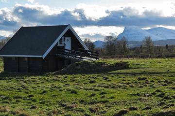 Tyrishølt en delvis skyet sommerdag, med grønt gress utenfor og snøkledde fjell i horisonten.