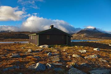 Sulebu en fin høstdag. Hytta ligger rett ved et lite vann, og fjelltoppene troner i bakgrunnen