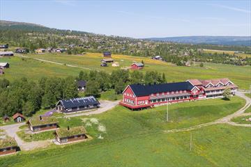 Dronenfoto eines roten Holzhotels in einer grünen Wiesenlandschaft