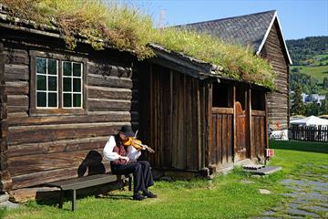 Spelemann spiller fele utenfor gammel bygning en sommerdag.