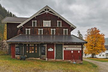 An old farm building with a farm store, a lawn, driveway and a yellow, autumn-coloured maple tree