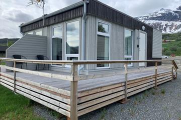 Ein kleines, viereckiges Gebäude mit Apartments, einer rundumgehenden Veranda und Bergen im Hintergrund