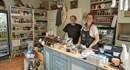 The owners of the store standing behind the counter of the small, cosy shop.The shelves are filled with delicious local food.