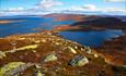 On the summit at Gravolskampen with bright green lichen-covered rocks. A far view over open mountain terrain and lakes.