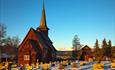 En stavkirke i en snødekt kirkegård i vintersolskinn.