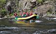 A yellow raft on a river passes a rock face