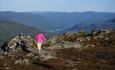 En jente i rosa genser på tur langs en fjellside med vid utsikt bakenfor.