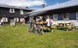 Fahrradfahrer genïeßen einen Snack an Picknicktischen auf dem Rasen an einer Mountain Lodge