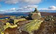 The summit cairn at Gravolskampen with bright green lichen-covered rocks. A far view over open mountain terrain and a large lake.