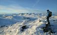 A person standing on the summit a midwinter day and enjoying the view to the high peaks of Jotunheimen.