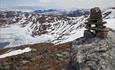 Eine Steinwarte mit einem weißen V weist den Weg zum Horntind. Es ist Frühsommer, und im Gebirge liegt noch viel Schnee.