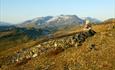 Mykt kveldslys over en varde langs en sti med høye fjell i bakgrunnen.